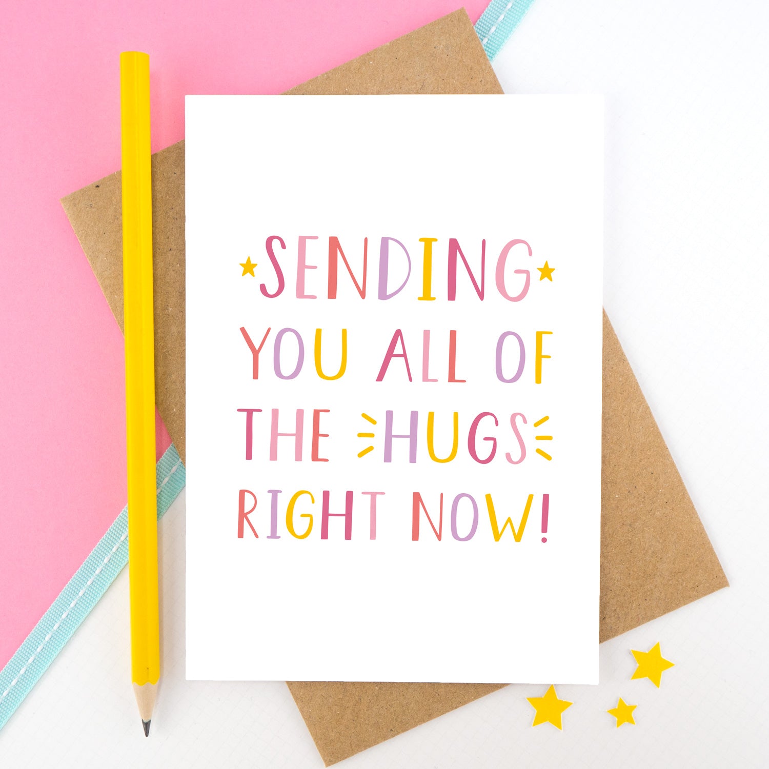 Sending you all of the hugs right card photographed on a pink and white background with a teal ribbon and a bright yellow pencil. This image shows the letters in a pinks, yellow and lilac palette.