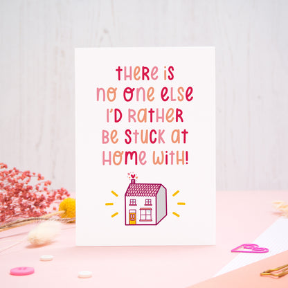 The 'stuck at home with you' card photographed standing up against an off white background with flowers, buttons and paperclips at the base of the card.