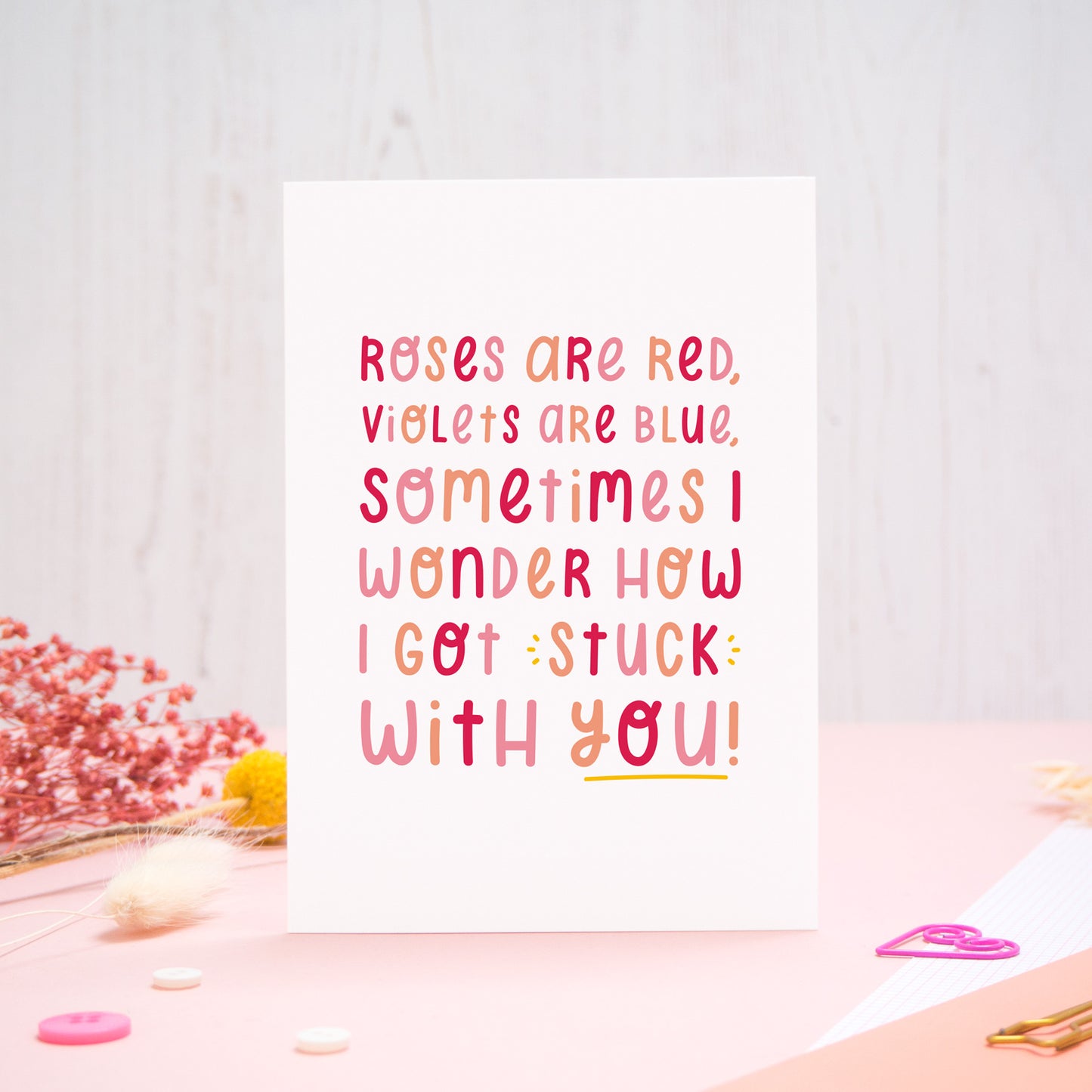 The 'stuck with you' card photographed standing up against an off white background with flowers, buttons and paperclips at the base of the card.