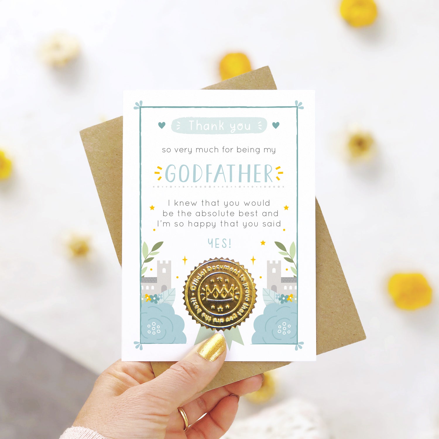 A ‘thank you for being my godfather’ certificate card with a shiny gold seal in the blue colour palette being held over a white background with yellow and natural flowers.