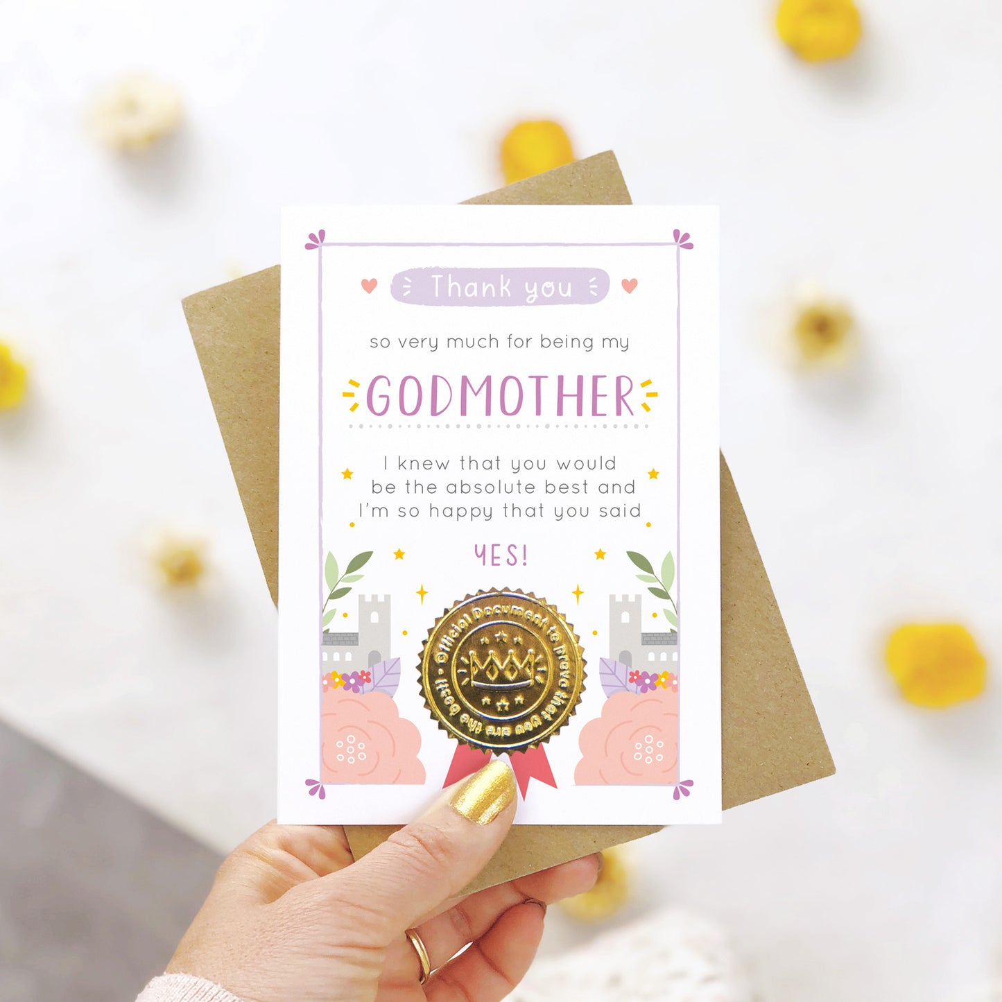A ‘thank you for being my godmother’ certificate card with a shiny gold seal in the purple colour palette being held over a white background with yellow and natural flowers.
