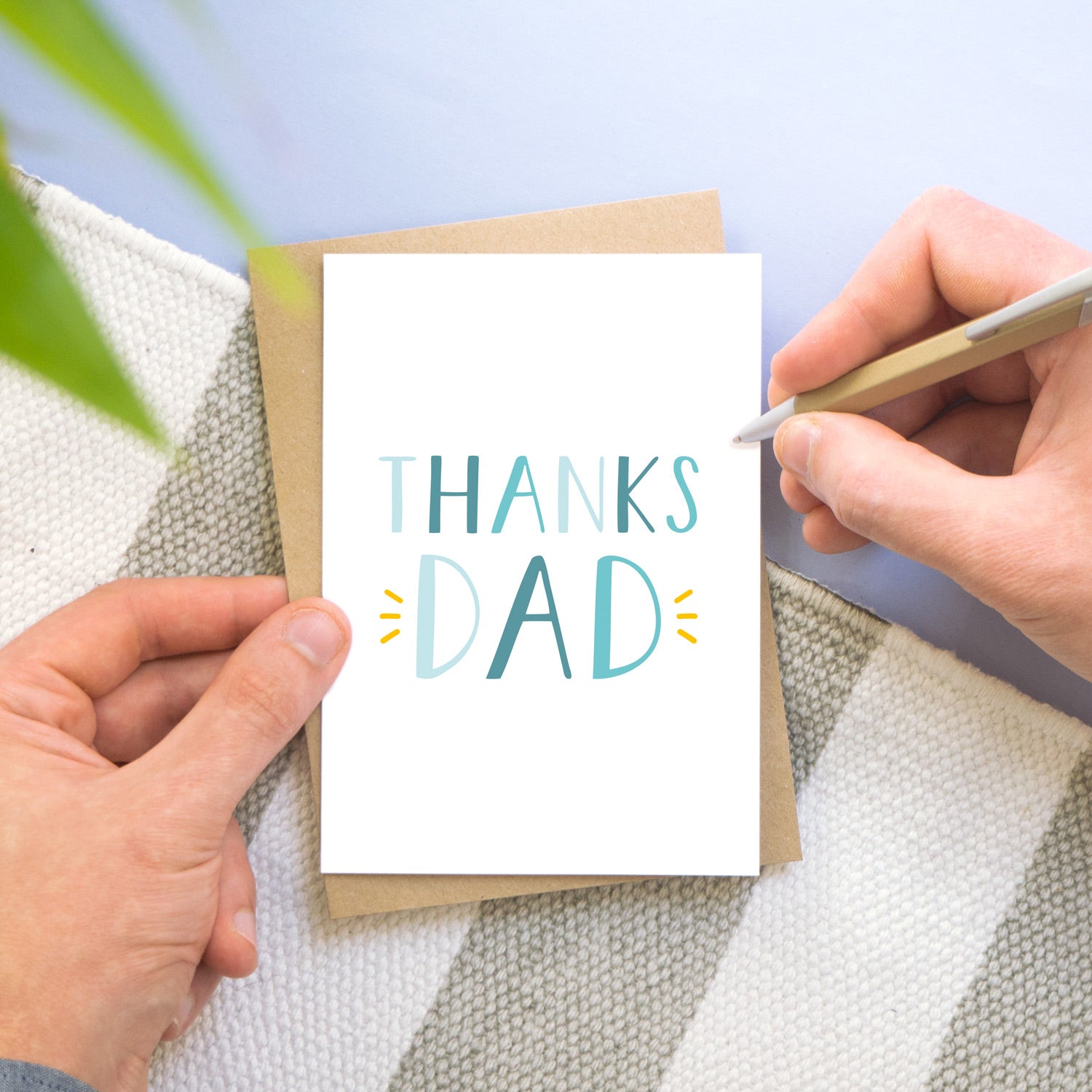 Thanks Dad! A simple typographic card being held by a man on a grey, white and blue background. The text is in varying shades of blue and with a pop of yellow around the word 'dad'.