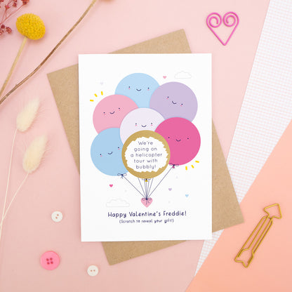 A personalised Valentine’s scratch card photographed on a pink background with floral props, paper clips, and buttons. This card shows the pink & lilac colour scheme and the golden circle has been scratched off to reveal the secret message!