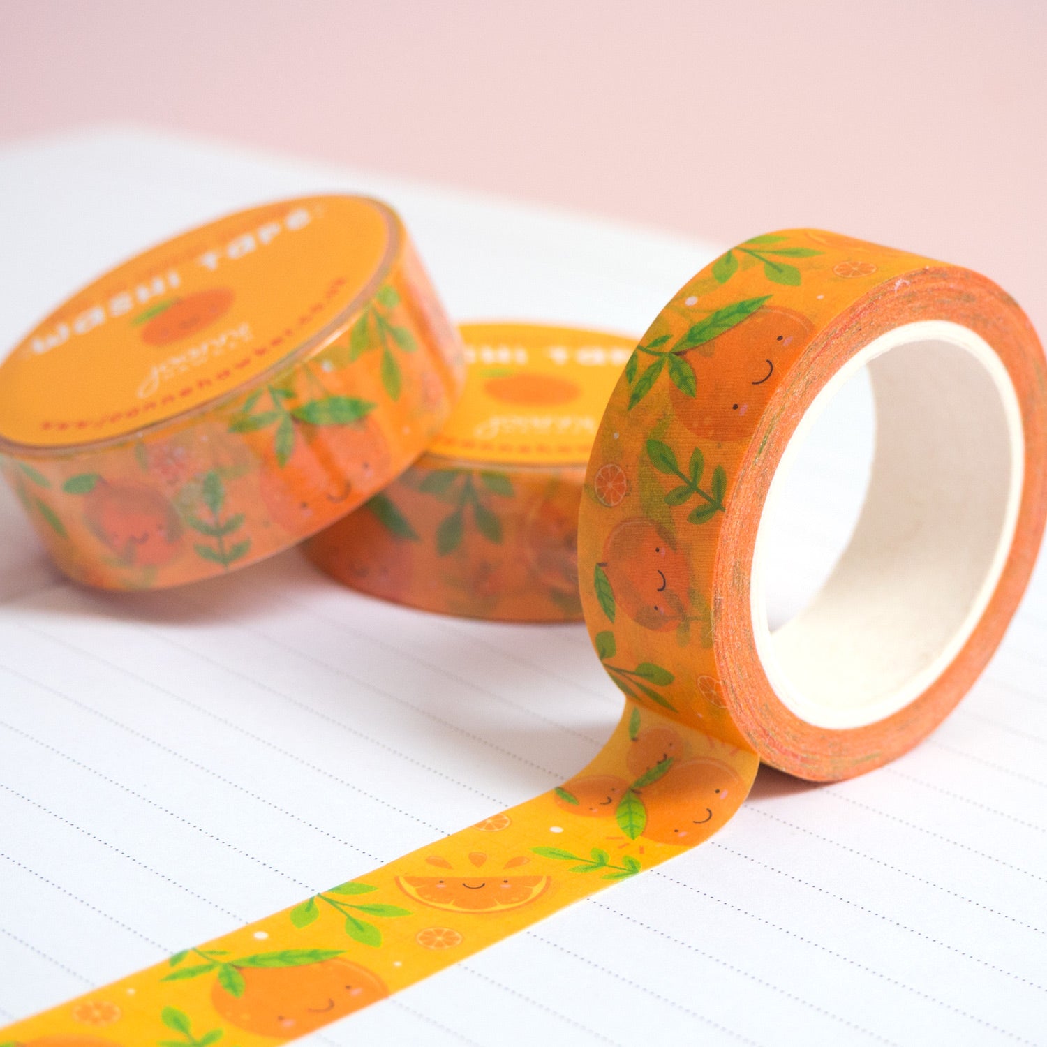 A roll of orange satsuma washi tape unravelling on a notebook with stacks of paper tape in the background.