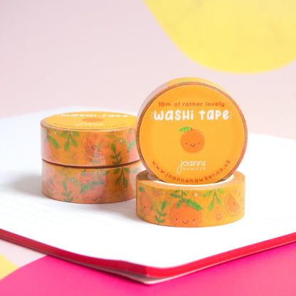 A stack of orange satsuma washi tape piled on top of a notebook with one roll facing forwards to show the decorative sticker.