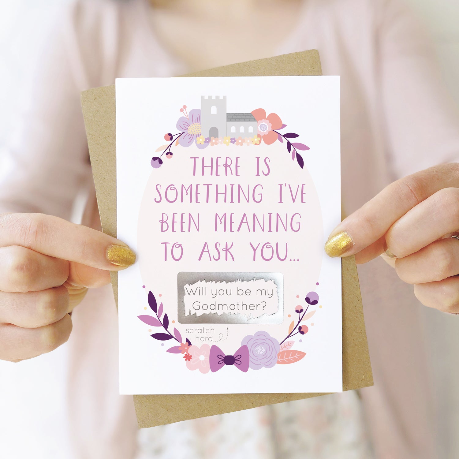 A will you be my godmother scratch and reveal card being held in front of a white dress and pink cardigan. The design features a church, simple florals and a scratch off panel in silver. This is the purple palette.