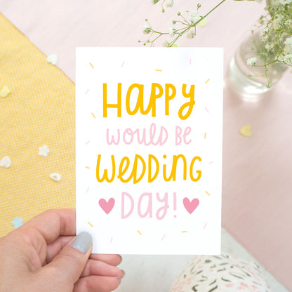 Happy would be wedding day card in orange and pink photographed in a hand against a pink, and yellow background with a hint of flowers.