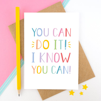 You can do it, I know you can! - Positive encouragement card photographed on a pick and white background separated with a teal ribbon. Also featuring a yellow pencil for scale. This version is in a rainbow colour palette.