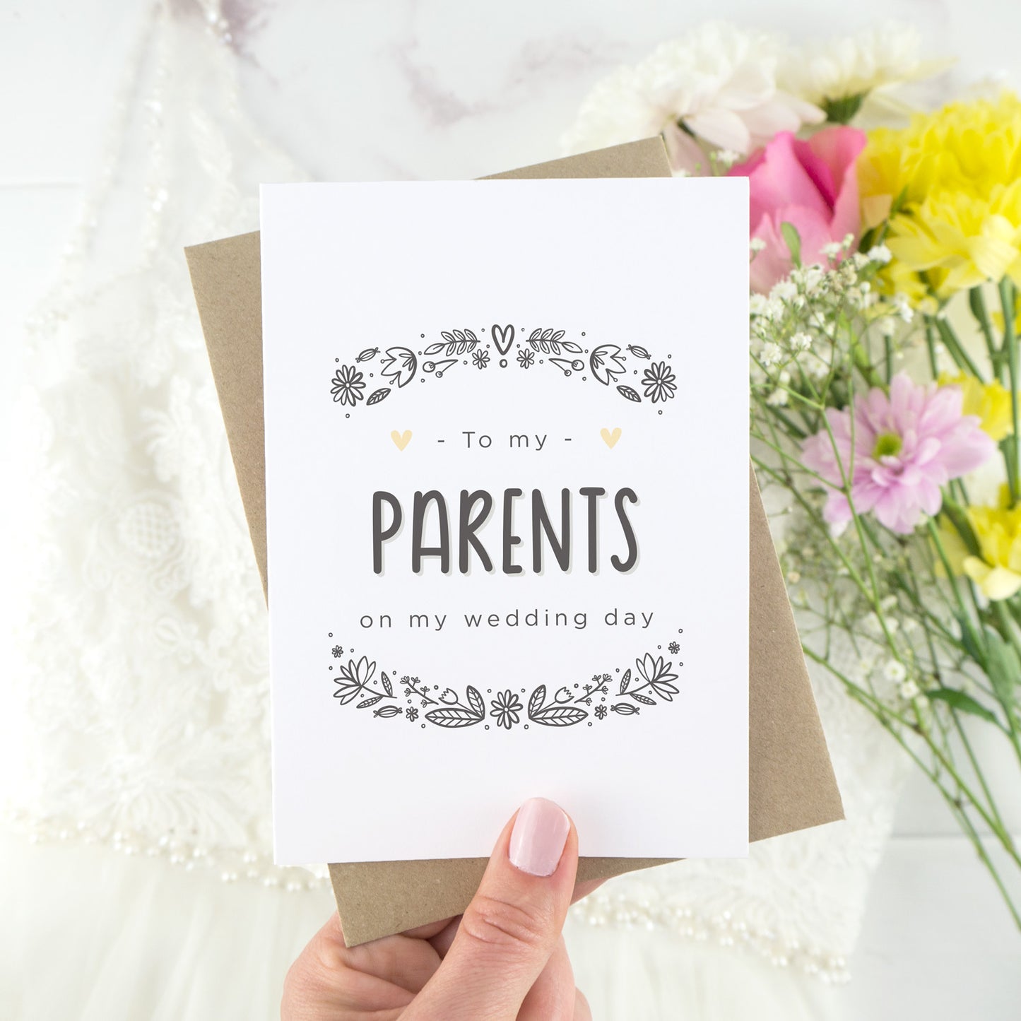 To my parents on my wedding day. A white card with grey hand drawn lettering, and a grey floral border. The image features a wedding dress and bouquet of flowers.
