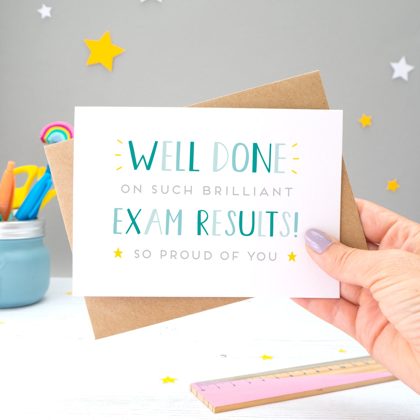 'Well done on such brilliant Exam Results! So proud of you. A congratulations card featuring my hand drawn type in varying shades of blue, with a bright yellow stars around the grey text.