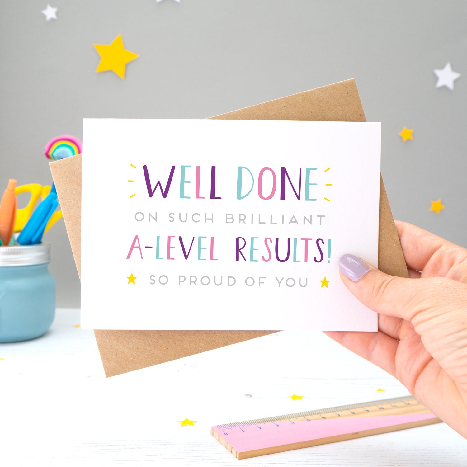 'Well done on such brilliant A-Level Results! So proud of you. A congratulations card featuring my hand drawn type in varying shades of pink, purple and blue, with a bright yellow stars around the grey text.