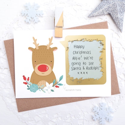 A christmas themed, write your own message scratch and reveal card featuring a red nosed reindeer, some winter florals a big shiny gold scratch panel with a hand written message.